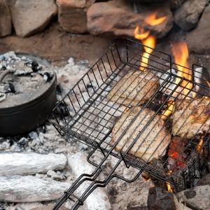 Grilling basket of burgers over campfire