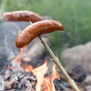 Juicy hot dog on stick over fire