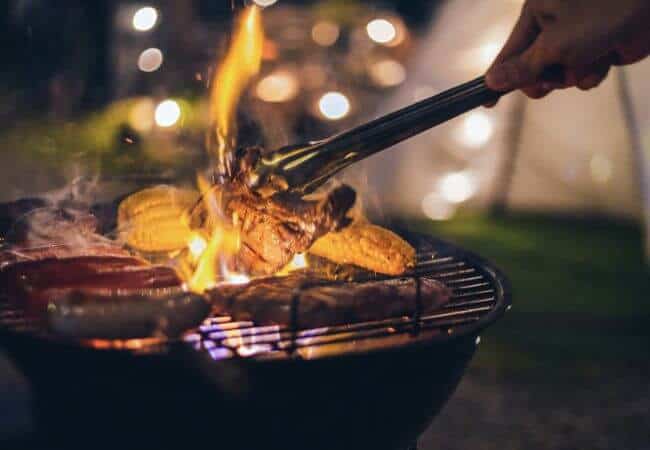 Grilling meat and corn with camping tent in background